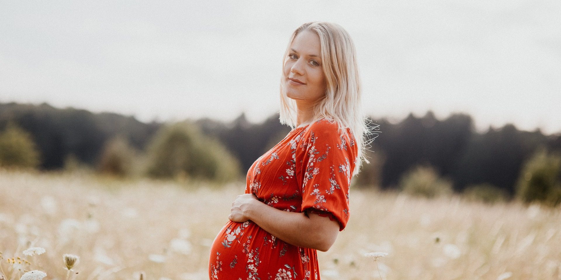 Pregnant woman in red dress poses in field.