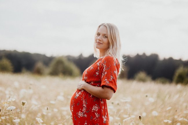 Pregnant woman in red dress poses in field.
