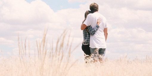 Couple stands in field hugging each other.