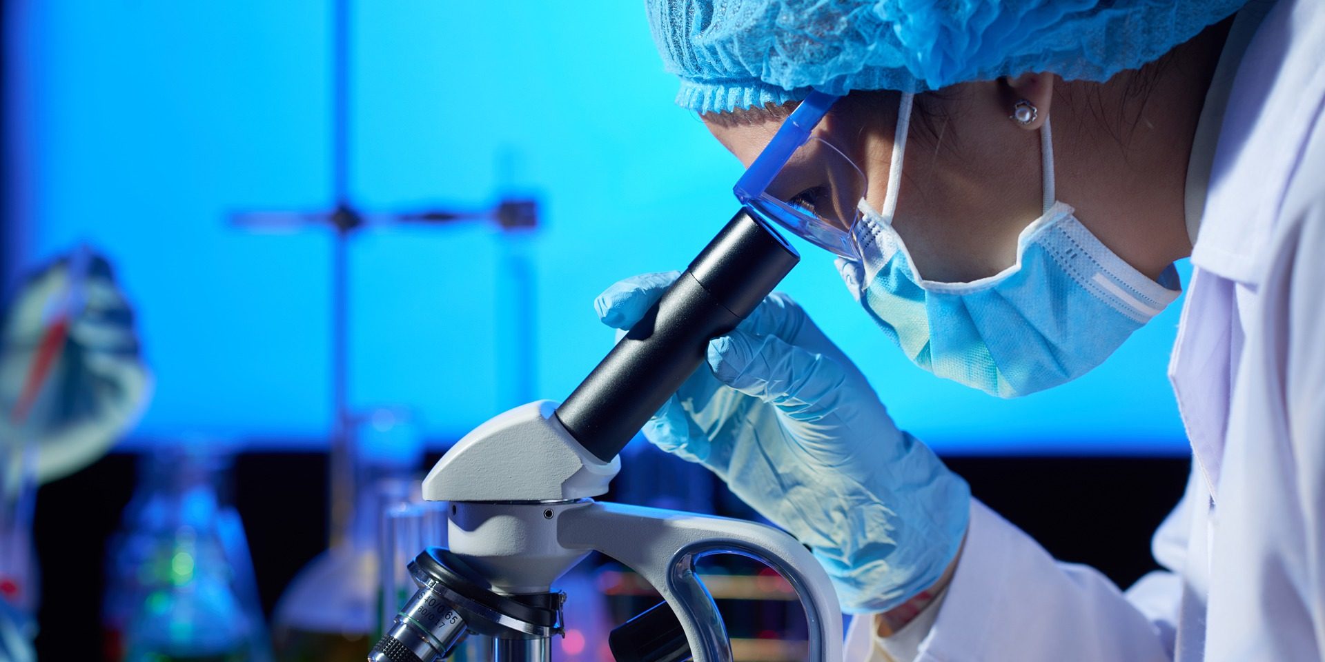 Scientist looks through microscope in lab.