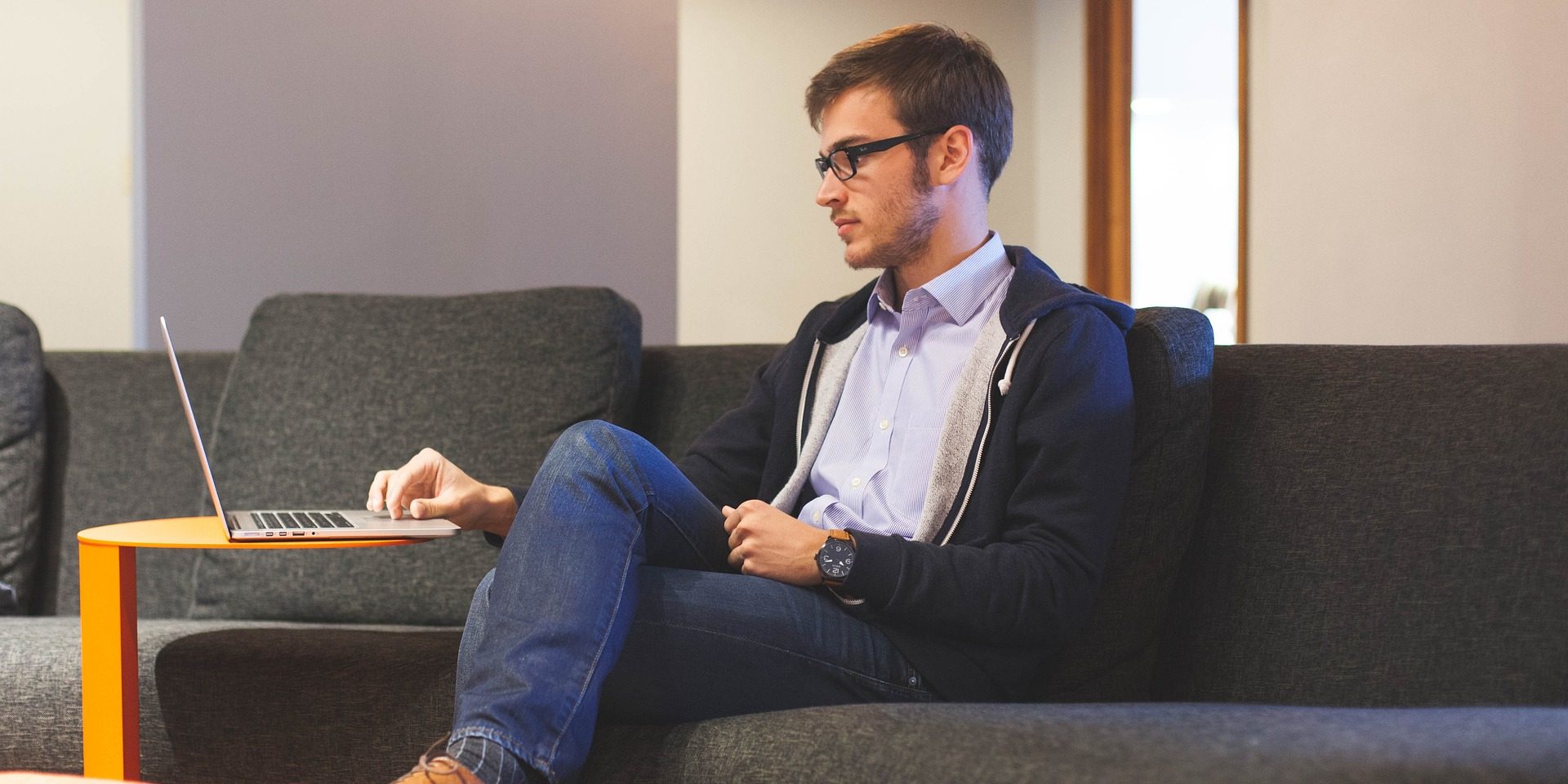 Man sits on couch with laptop on table in front of him.