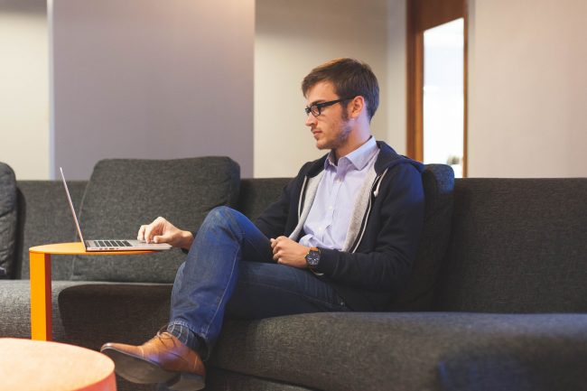 Man sits on couch with laptop on table in front of him.