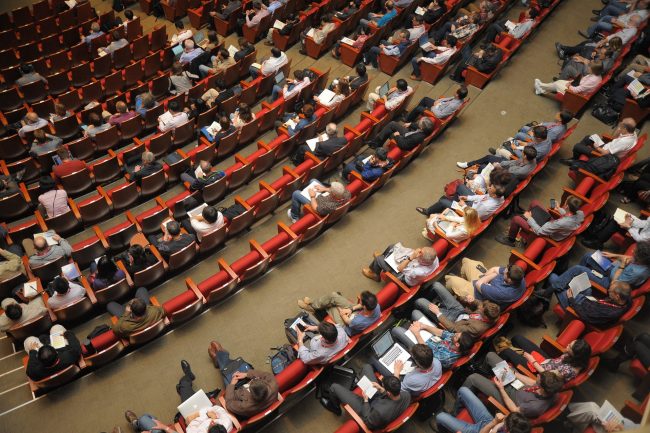 People sit in red chairs in auditorium for an event.