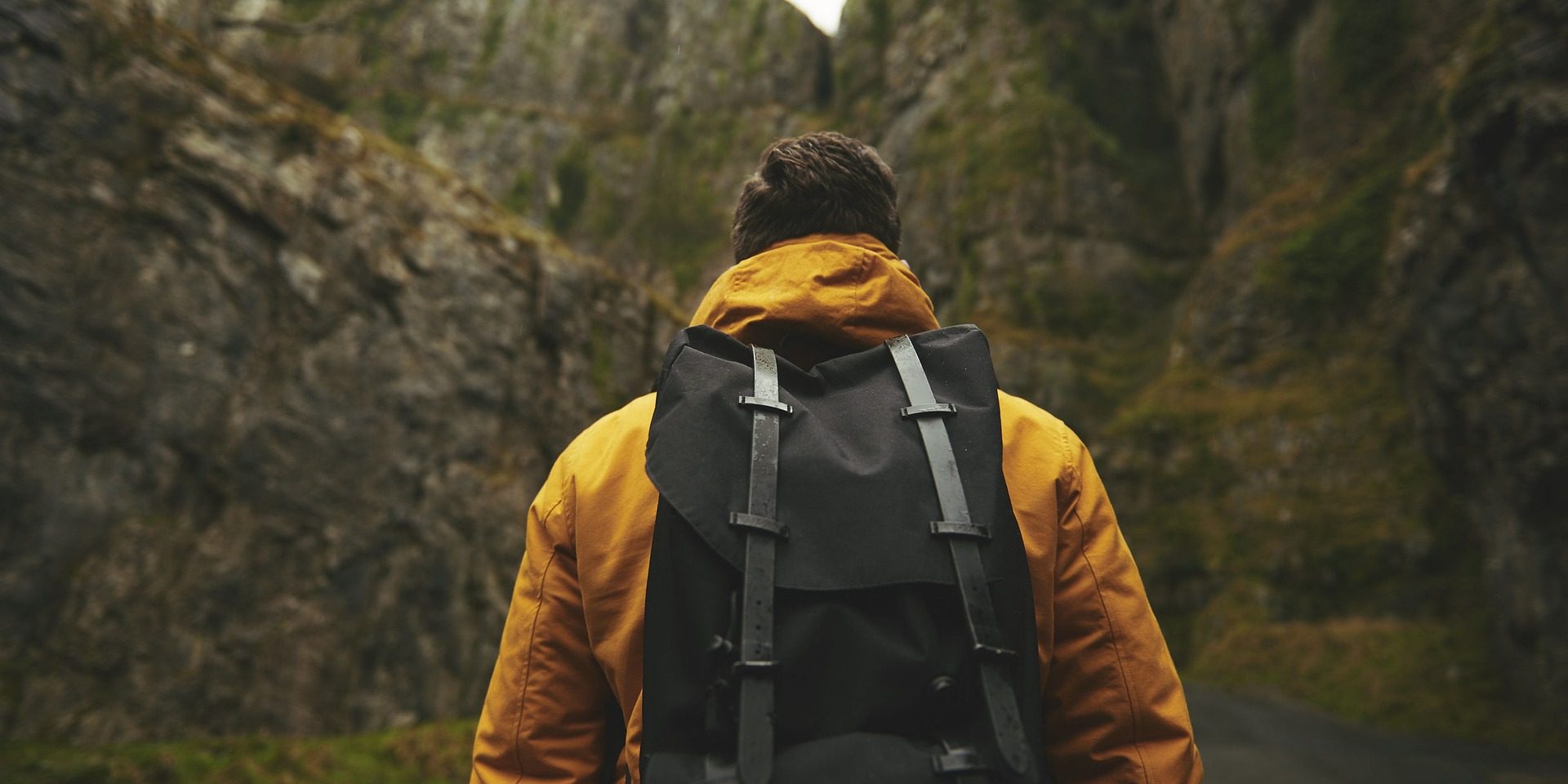Man wearing yellow jacket and backpack hikes mountain.