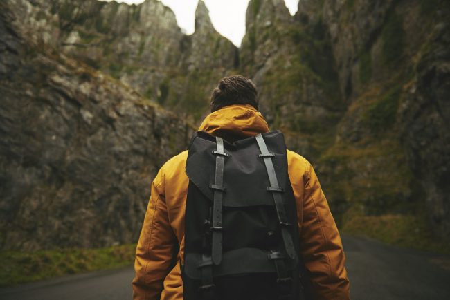 Man wearing yellow jacket and backpack hikes mountain.