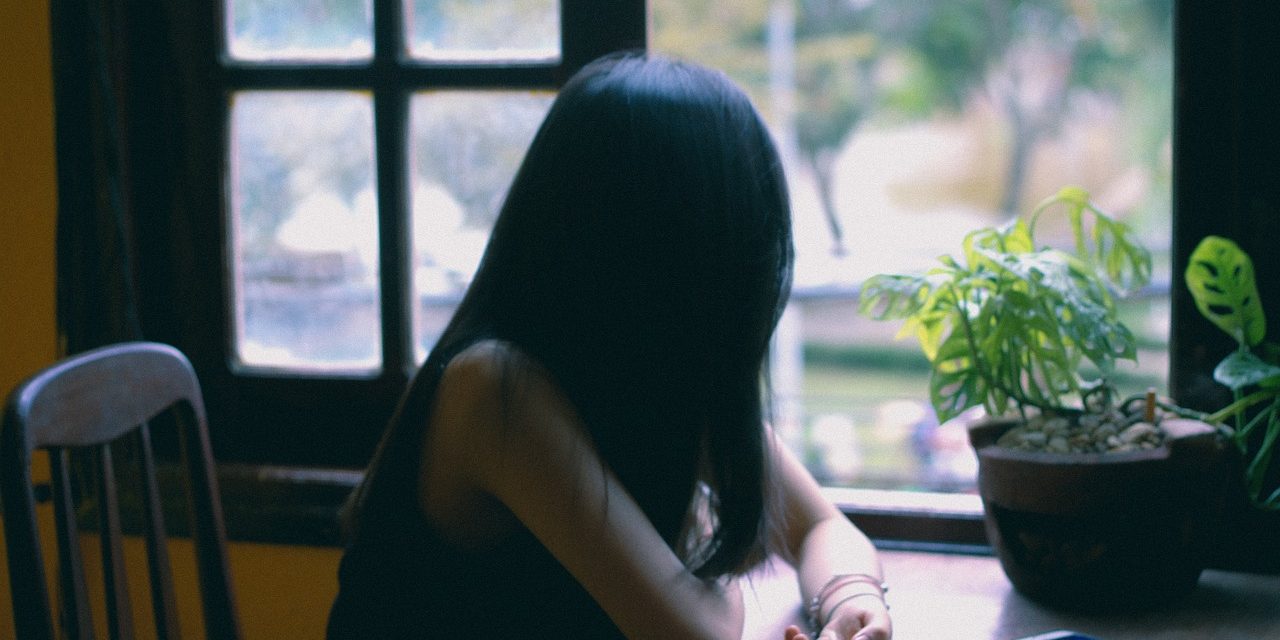 Woman sits at table looking out window