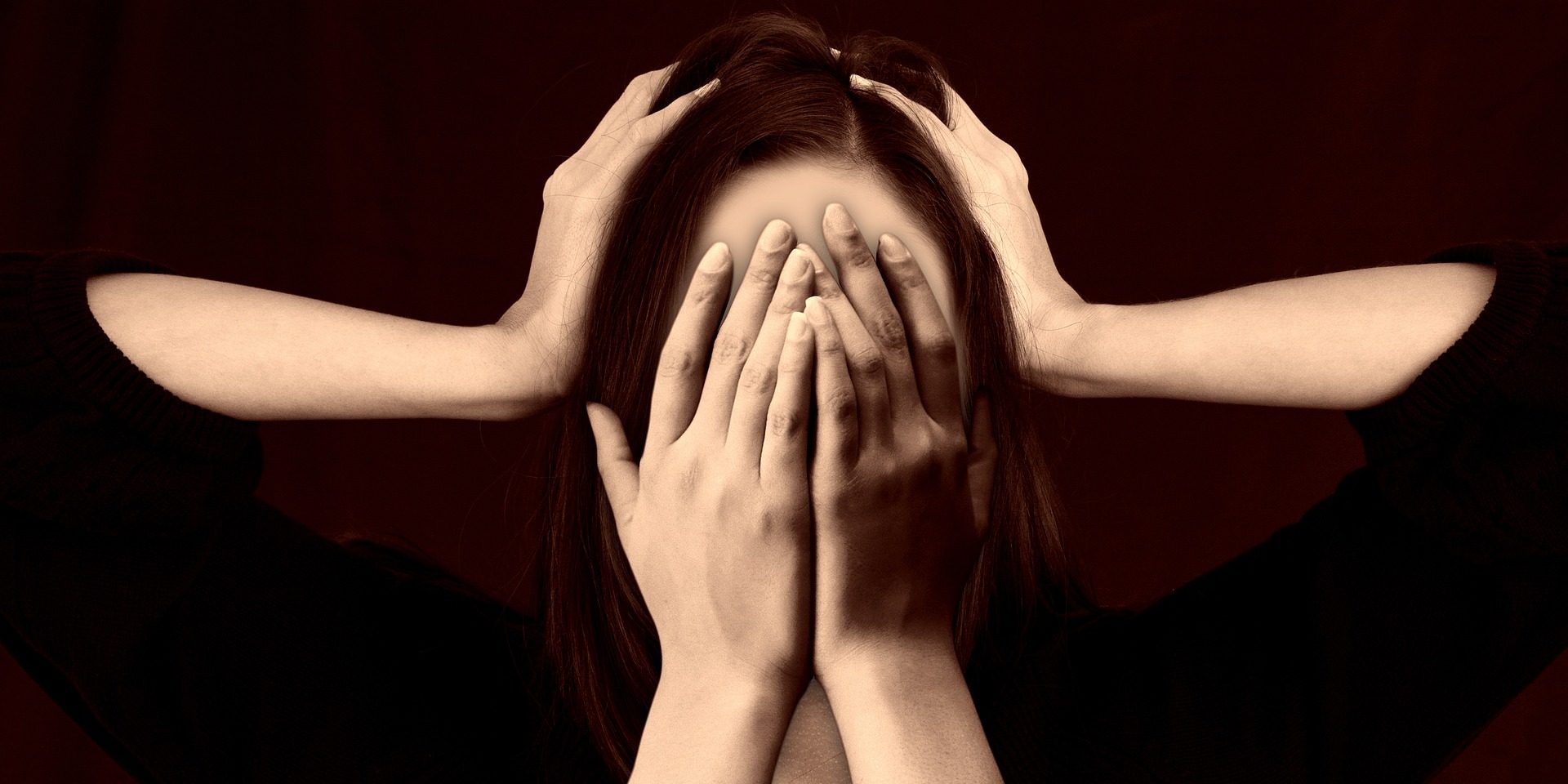 Woman pictured in black shirt with hands over her eyes and another set of hands over her ears.